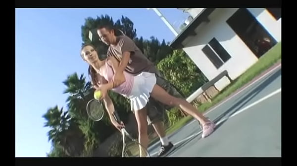 Cheerful brunette in a short skirt gives a guy a blowjob on the tennis court